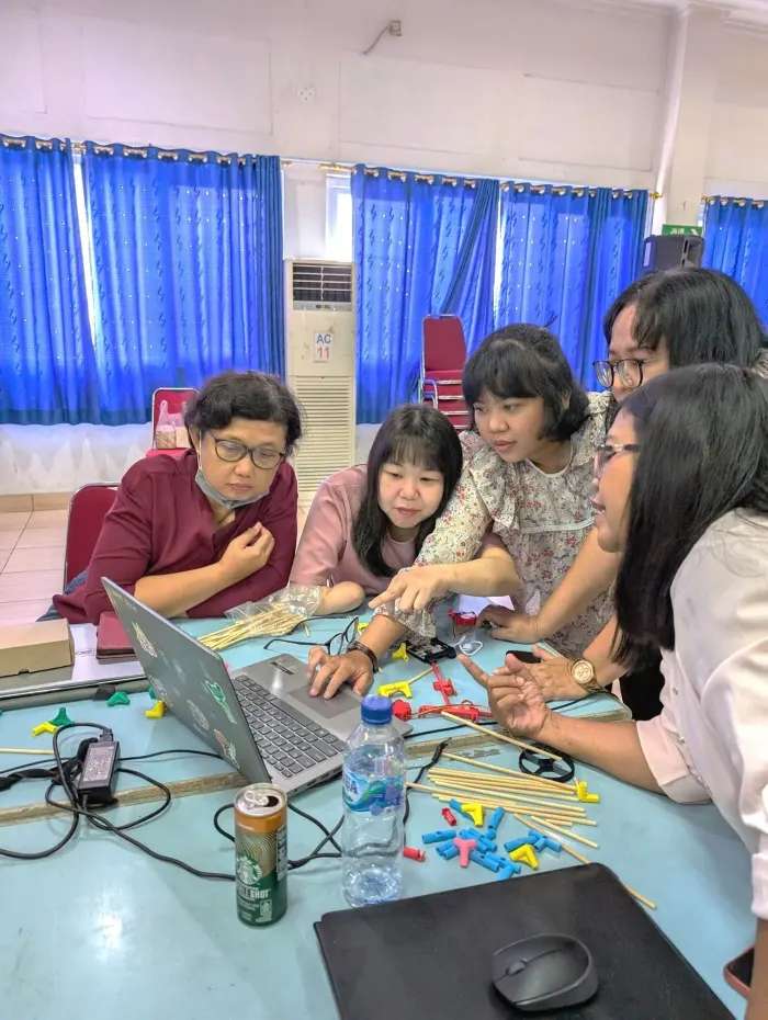 Teachers around a table covered in parts, working from a laptop